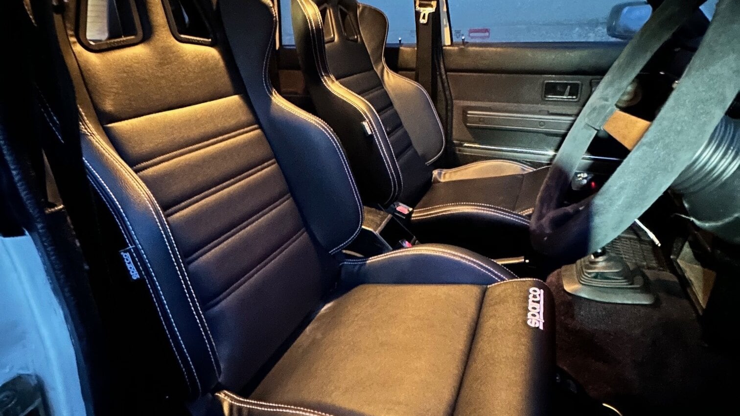Two black Sparco R100 vinyl reclining seats fitted in the front of a Volvo 240