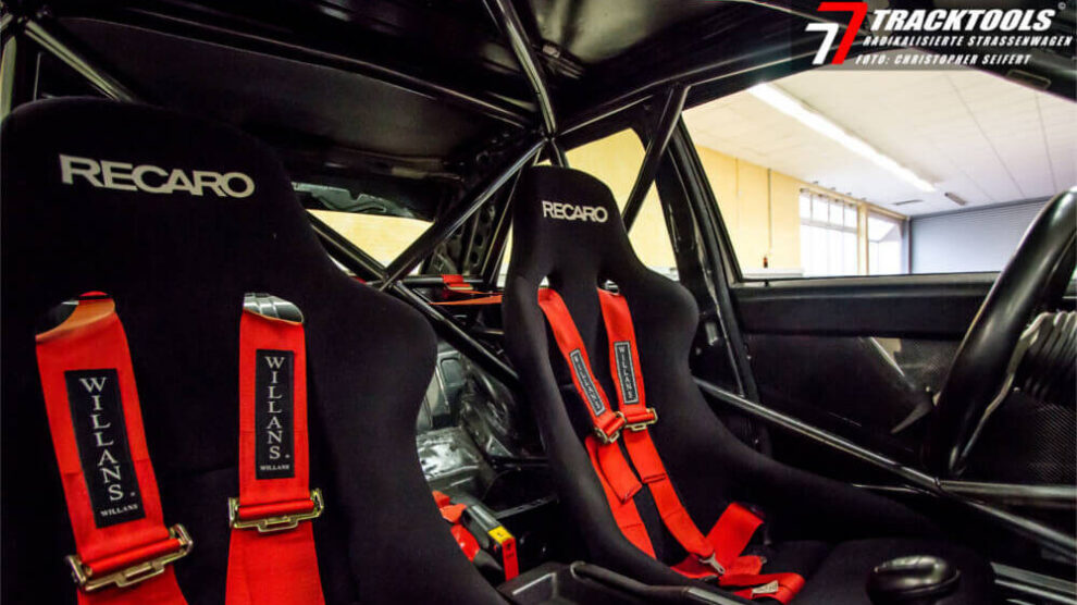 Red Willans harnesses on two black Recaro bucket seats in a car with a black roll cage