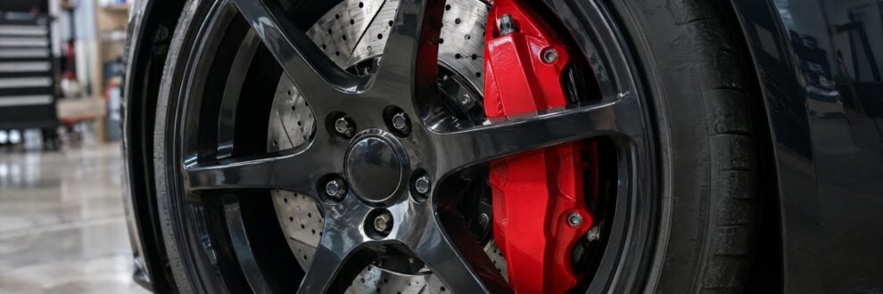 A red big brake caliper and drilled disc behind a black wheel