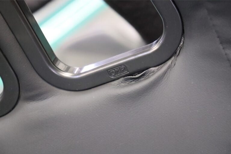 Illustration of the fabric around a black plastic harness slot surround with the lower edge popped out from under the rim