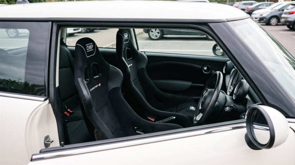 A pair of black velour OMP Champ-R bucket seats fitted in a white Mini R56, seen through the open driver window with the door closed