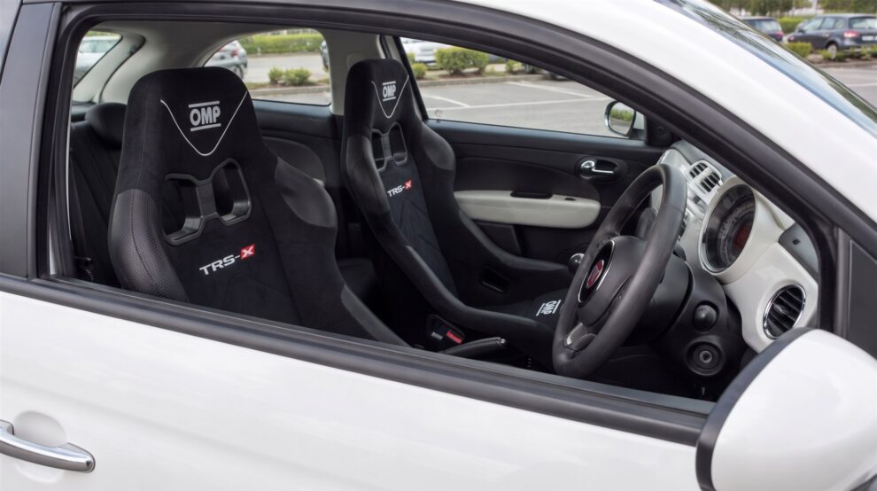 A pair of black OMP TRS-X bucket seats fitted in a white Fiat 500, seen through the open driver window with the door closed