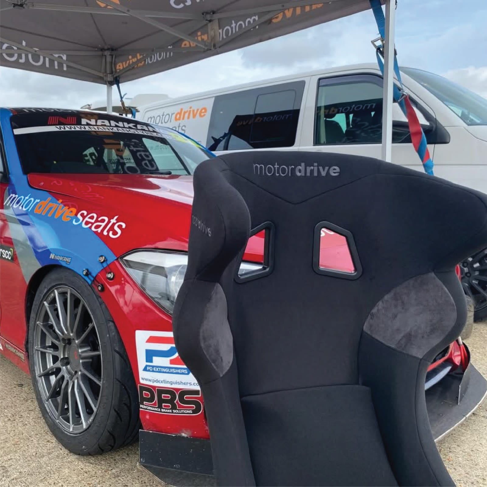 Motordrive head-support seat in a paddock beside a race car