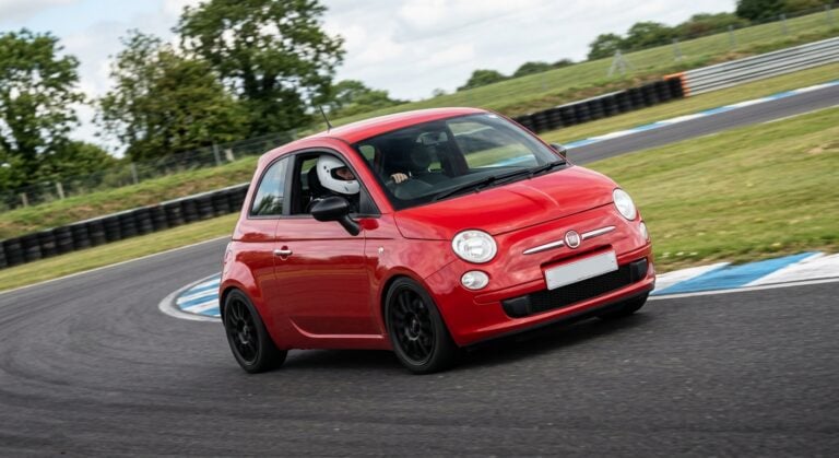 Fiat 500 cornering on a British race circuit with a helmeted driver visible at the wheel