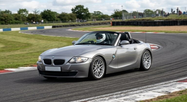Dark blue BMW Z4 E85 Roadster cornering on a British race circuit with a helmeted driver visible