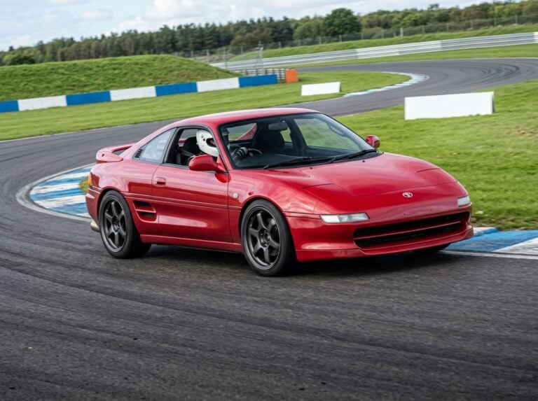 Red Toyota MR2 W20 (SW20) cornering on a British race circuit with a helmeted driver visible